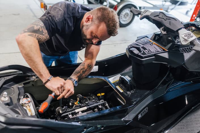 A technician working inside the engine compartment of a Sea-Doo personal watercraft